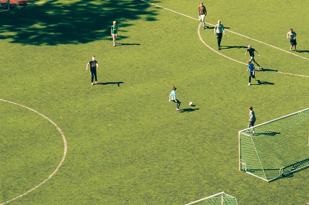Football players on a sunlit grass pitch seen from above