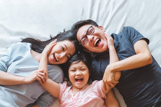Laughing family with a child lying together on a bed