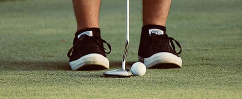 Golfspelare står vid en golfboll på en green